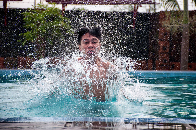 Portrait of man splashing in swimming pool