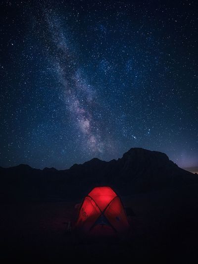 Illuminated tent on mountains against star field in sky at night