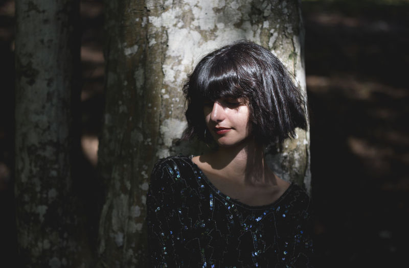 Young woman with short hair standing by tree trunk in forest