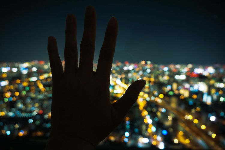 Hand silhouette cityscape against sky at night