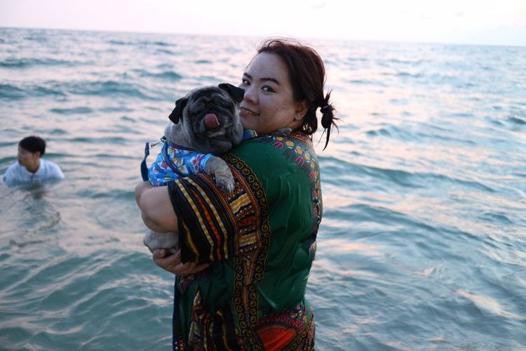 Portrait of woman holding pug at beach