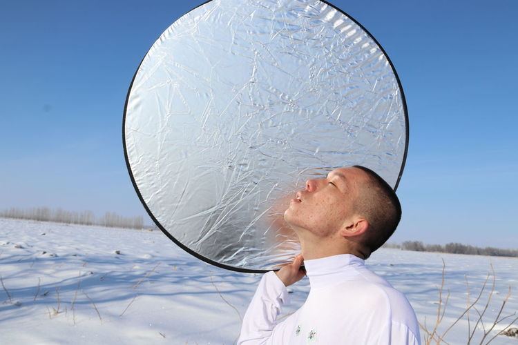 Young man with foil against clear sky during winter