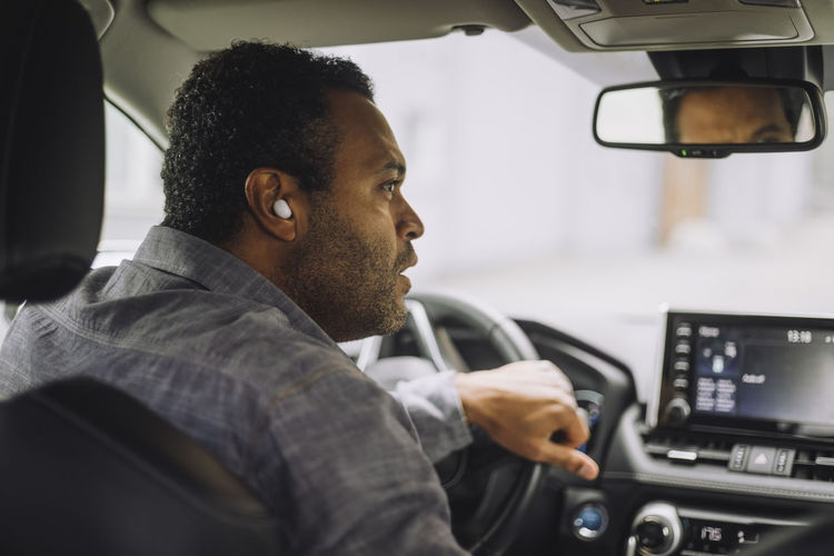 Male professional wearing wireless in-ear headphones driving car
