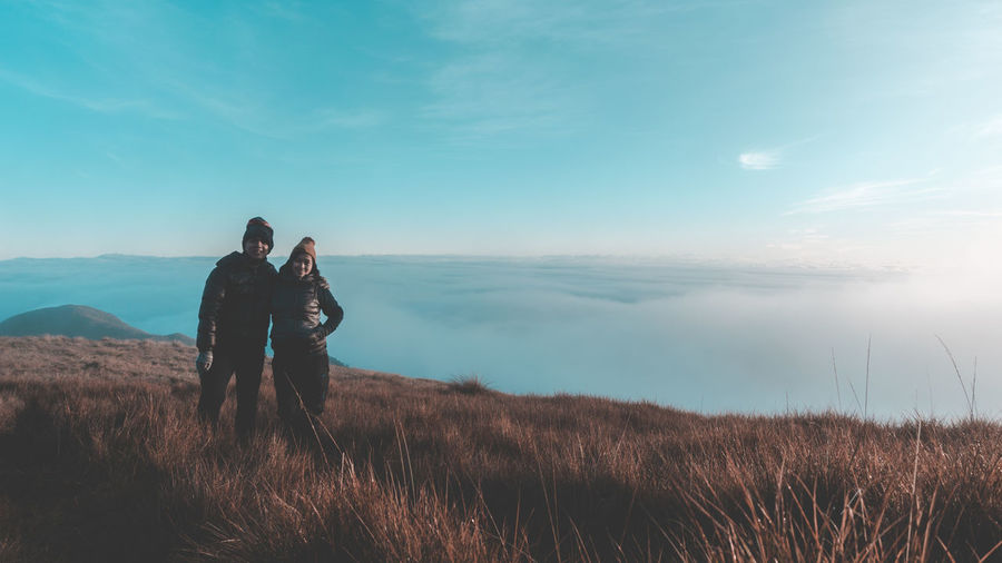 Couple standing on cliff against cloudy sky