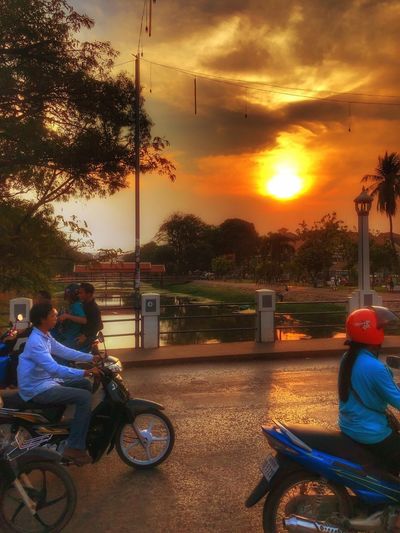 People riding motorcycle against sky during sunset
