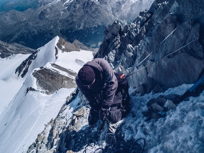 High angle view of hiker climbing rock against snowcapped mountain