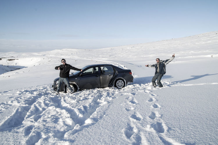 Portrait of male friends gesturing while standing by car on snow covered field