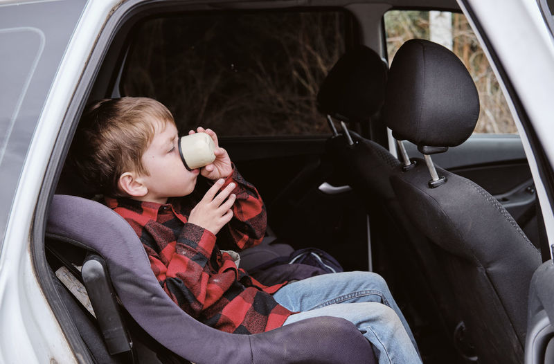 Autotrip with children. travelling by car. boy drinks from a cup in the car