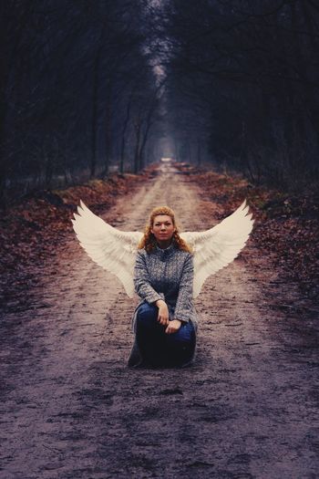 Portrait of woman with costume wings crouching on road amidst forest