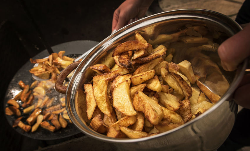 Cropped hand of person holding fried potatoes in container