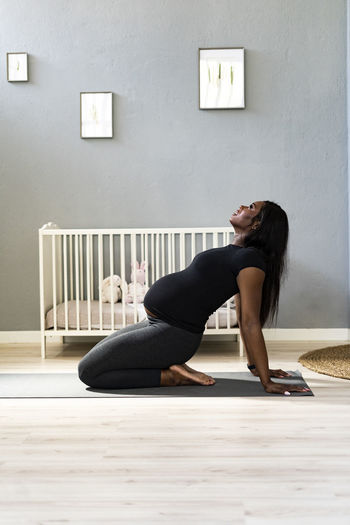 Young pregnant woman leaning back while practicing yoga in bedroom