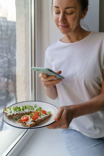 Woman photographing food in plate with mobile phone at home