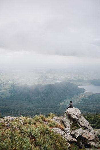 Hiker sitting on rocks against cloudy sky during foggy weather