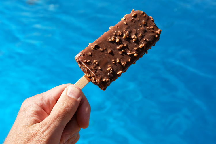 Close-up of hand holding chocolate ice cream against swimming pool