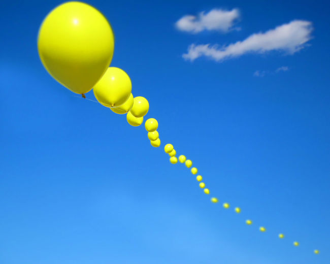 Low angle view of yellow balloons against blue sky on sunny day
