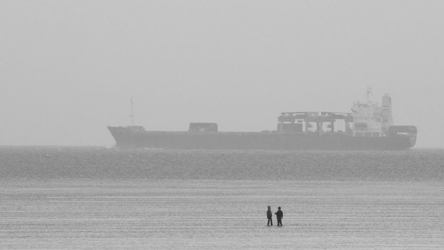 Two boys playing in the wadden sea with container ship in the background