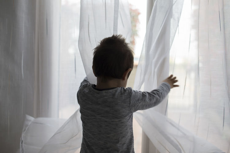 Rear view of boy standing by curtain at home