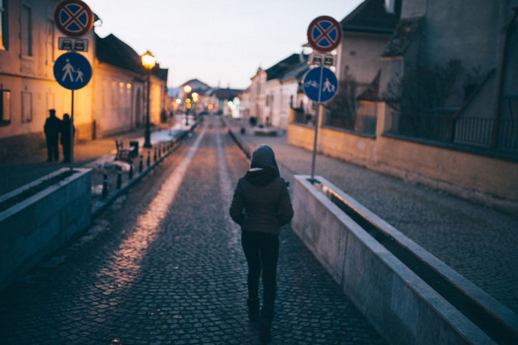 Rear view of woman walking on cobbled street during sunset