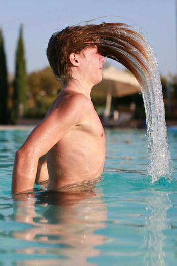 Side view of shirtless boy shaking his hair in swimming pool