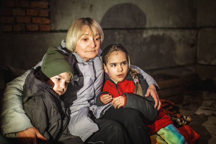 Grandmother hugs little ukrainian kids, they sit out attack of russian aggressor in bomb shelter