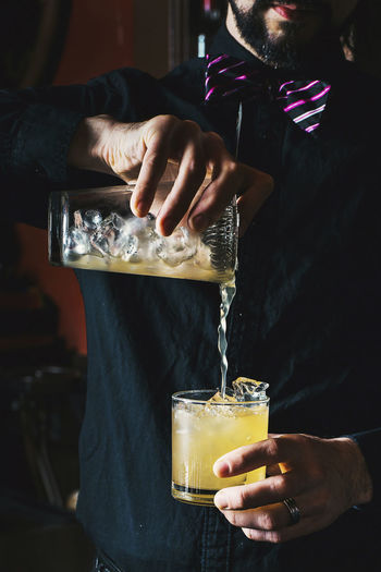 Midsection of bartender preparing drink while standing in bar