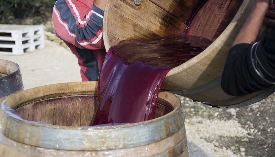 Cropped image of men pouring red wine in cask at warehouse