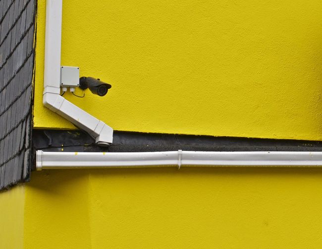 Low angle view of security camera on yellow wall