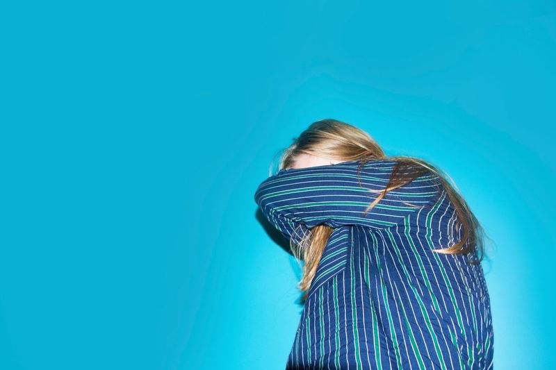 Woman covering face while standing against blue background