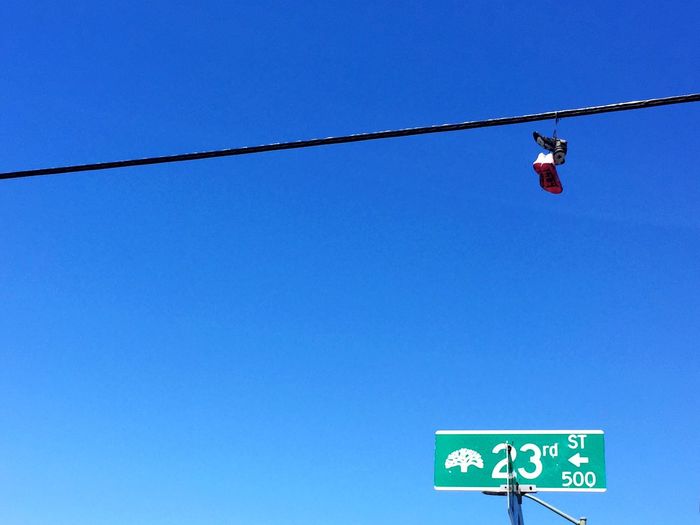 Low angle view of shoes hanging to cable against clear blue sky