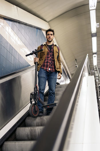 Man in stylish outfit with electric scooter in the mechanic stair of underground