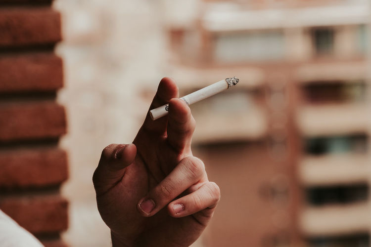Close-up of hand holding lit cigarette outdoors