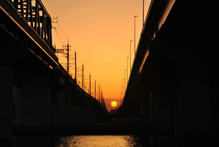 Silhouette bridge over river against orange sky