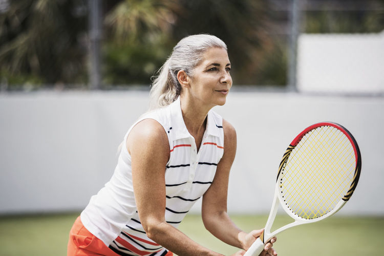 Determined mature woman playing tennis on court