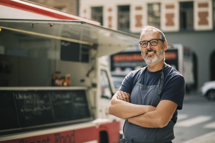 Portrait of confident chef with arms crossed standing by food truck on street