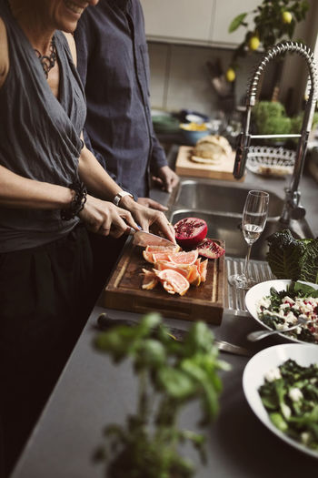 Midsection of mature woman cutting grapefruit while standing by man at kitchen counter