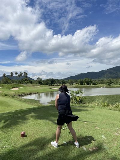 Rear view of woman standing on golf course against sky