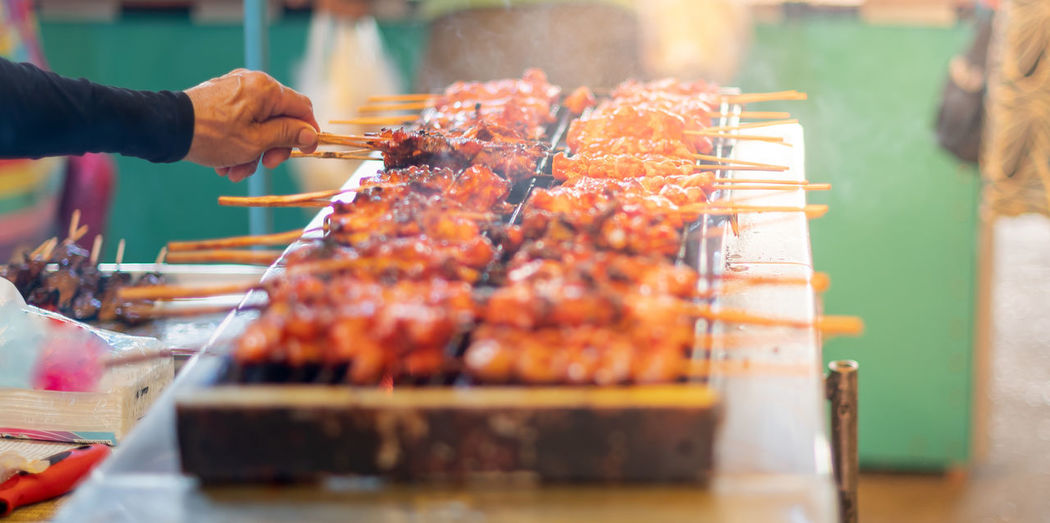 Male hand holding steel of meat grills kind of marinated meat in the aluminum pot with the charcoal