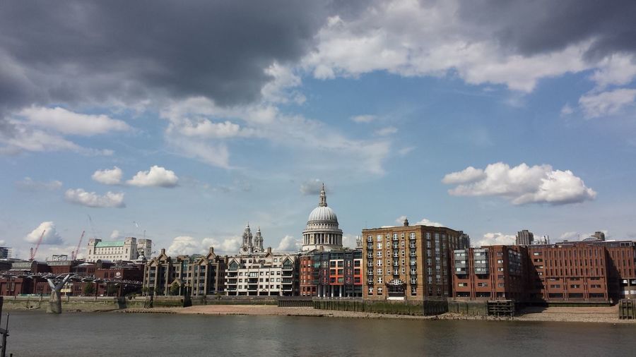 Millennium footbridge over thames river with st paul cathedral in city against sky