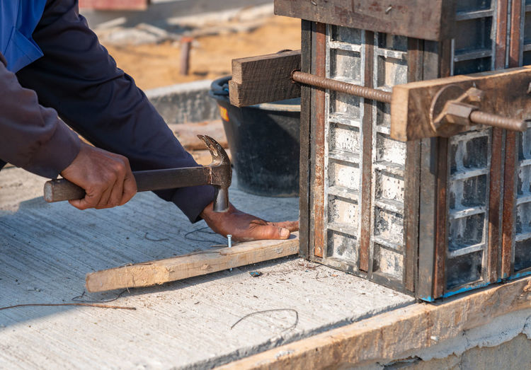 Workers drive concrete nails into wooden bars to support the concrete form work columns.
