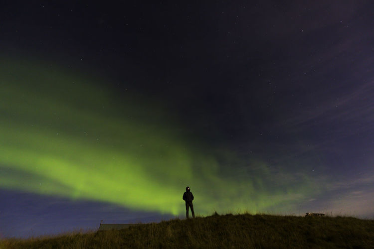 Silhouette man standing on field against aurora borealis at night