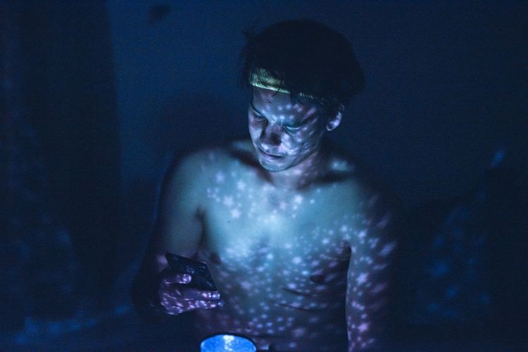 Shirtless man using mobile phone in illuminated room