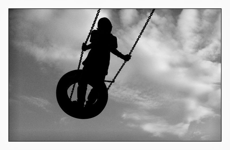 Silhouette boy swinging on tire swing against sky