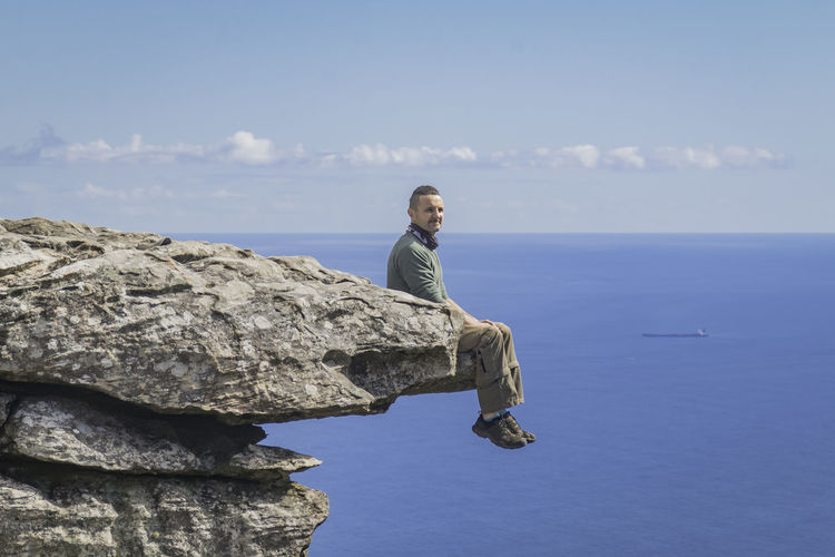 Man standing on rock by sea against blue sky