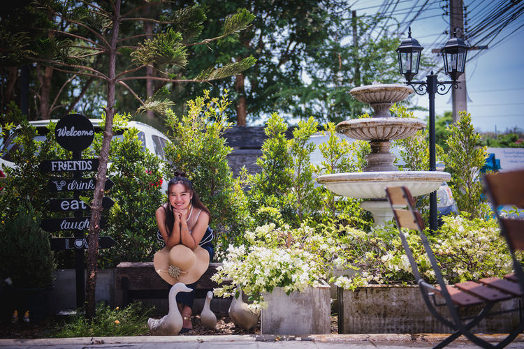 Young woman sitting by potted plants against trees