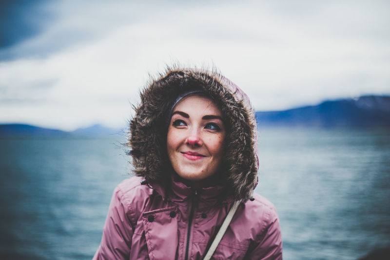 Smiling woman in warm clothes against sea 