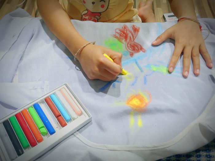 High angle view of girl drawing with chalk on white textile at home