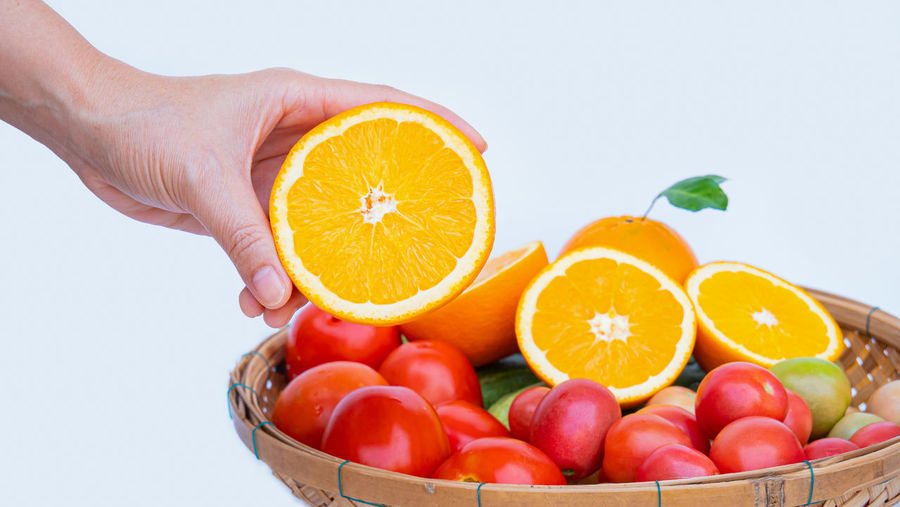 Close-up of hand holding orange fruit against white background