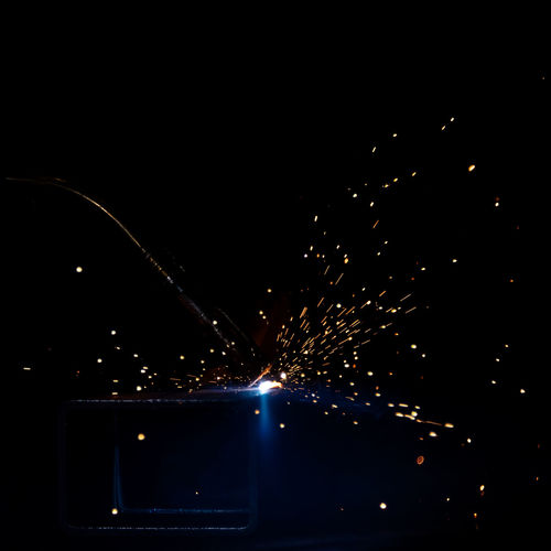 Closeup of mig welding torch on square tube metal with sparks on completely black background