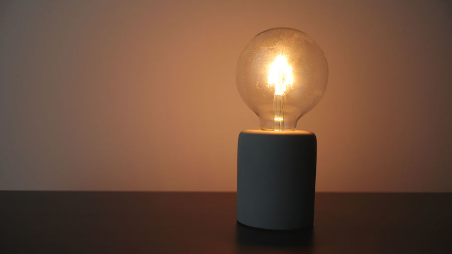 Close-up of illuminated light bulb on table against wall