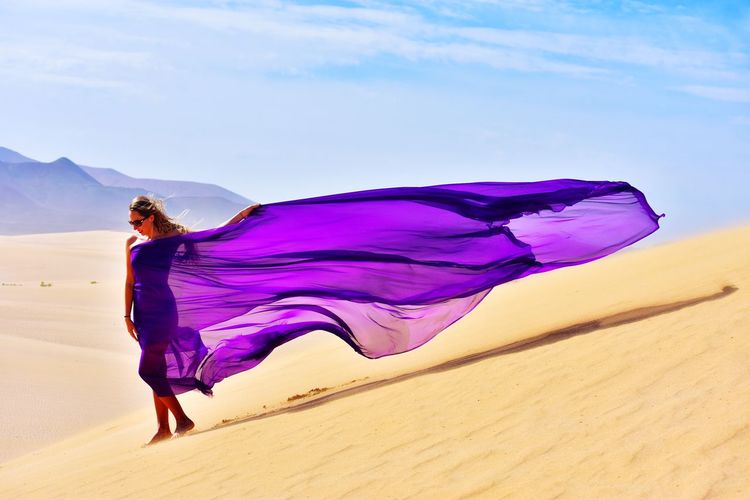 Woman wearing purple dress while standing at desert against sky